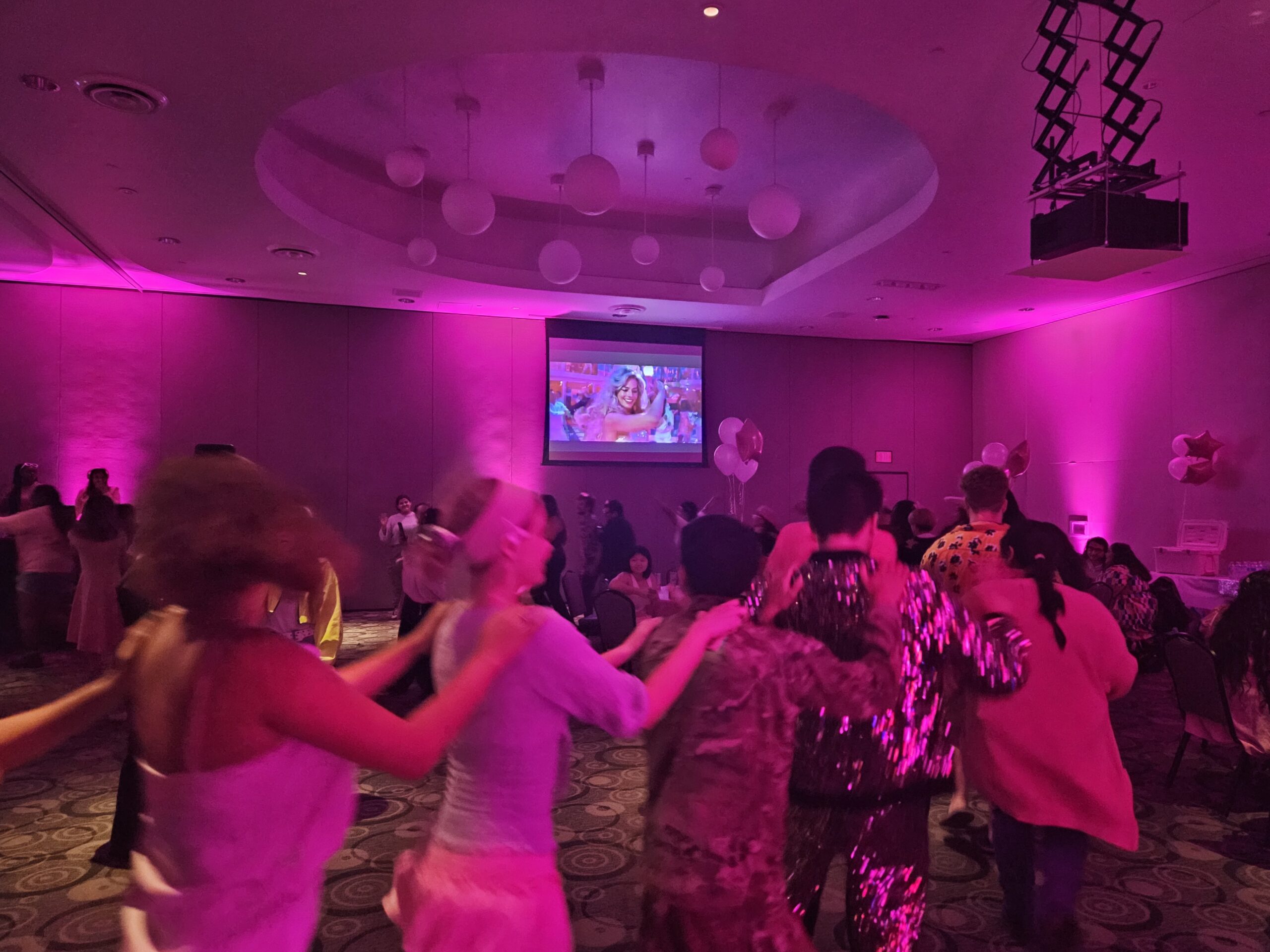 Photo of a room bathed in pink light with people dancing a conga line