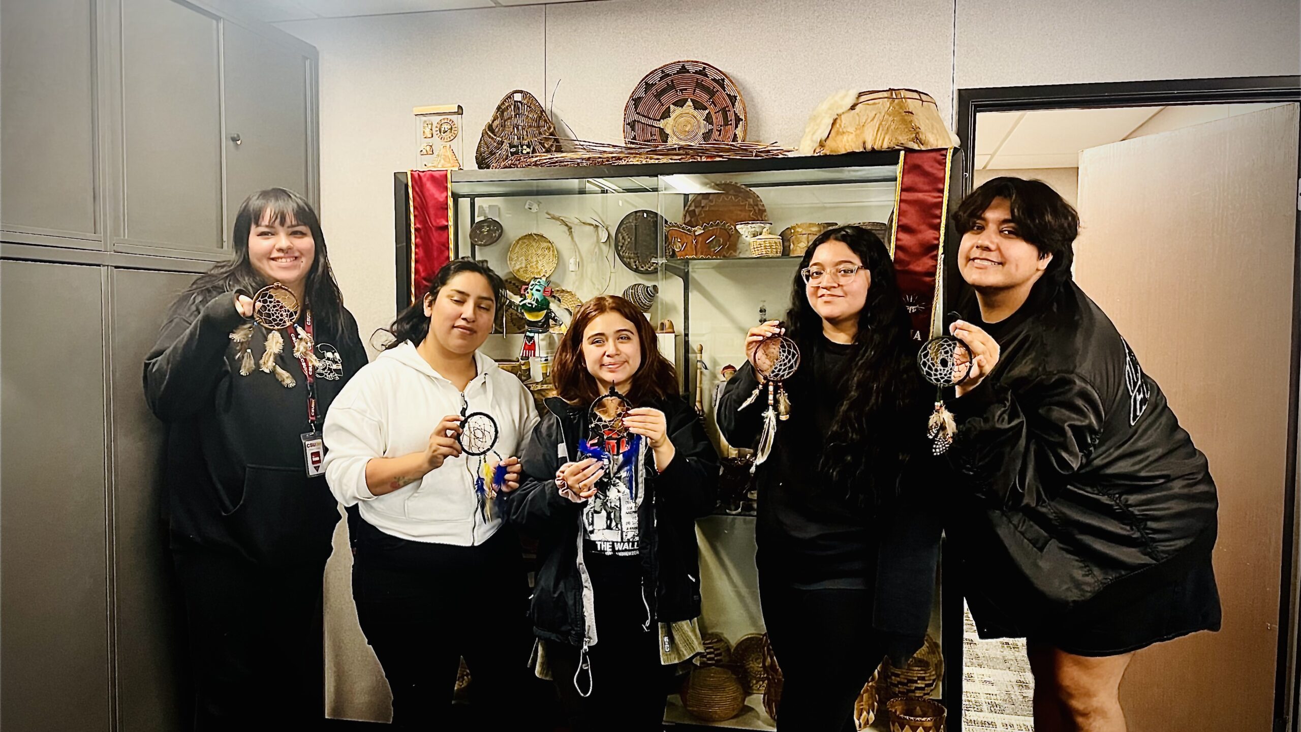 Photo of five people with handmade art in front of a display case.