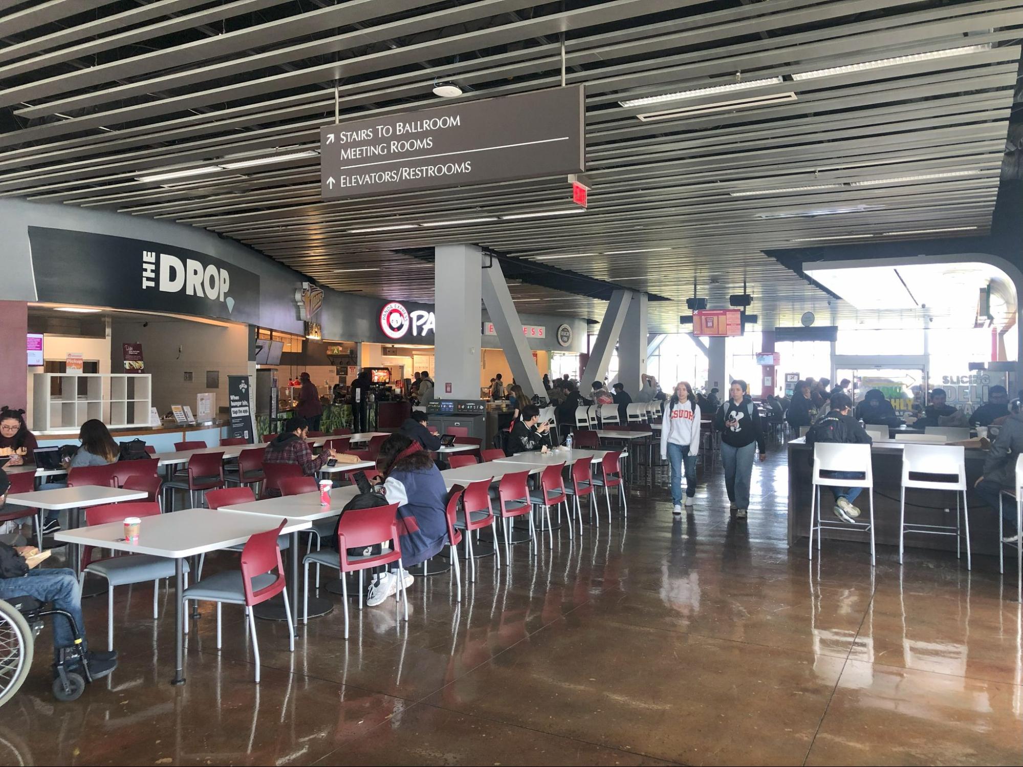 Photo of a cafeteria with red chairs and students.