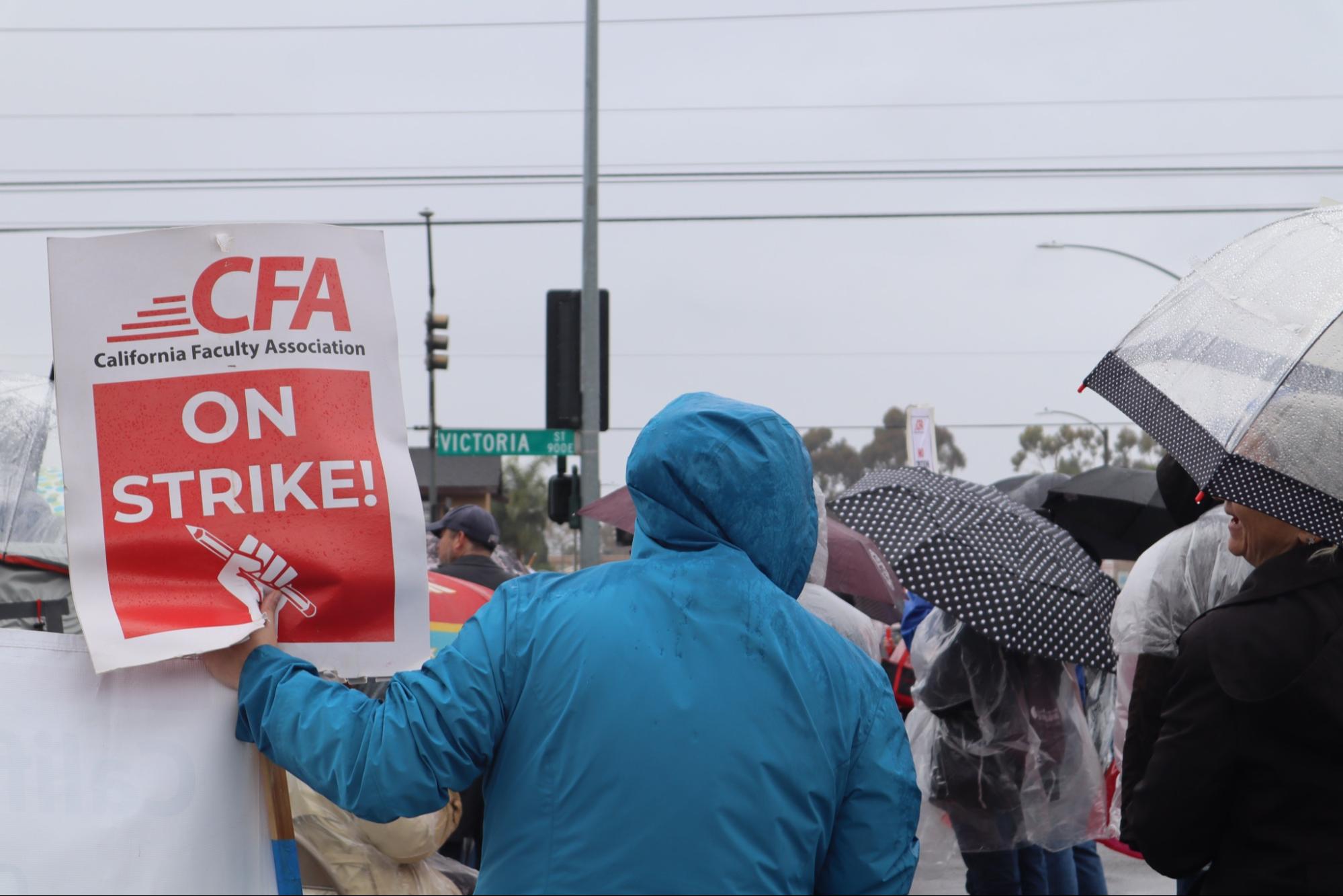 Photo of crowd in rain, person in blue jacked holding red "On Strike" sign