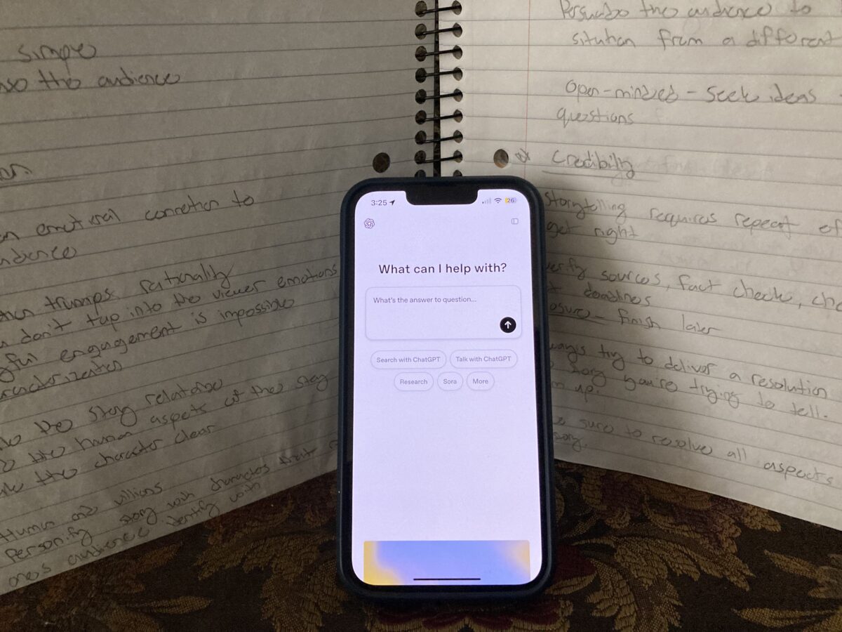 An iPhone with the ChatGPT app open leaning up against a notebook with hand-written notes.