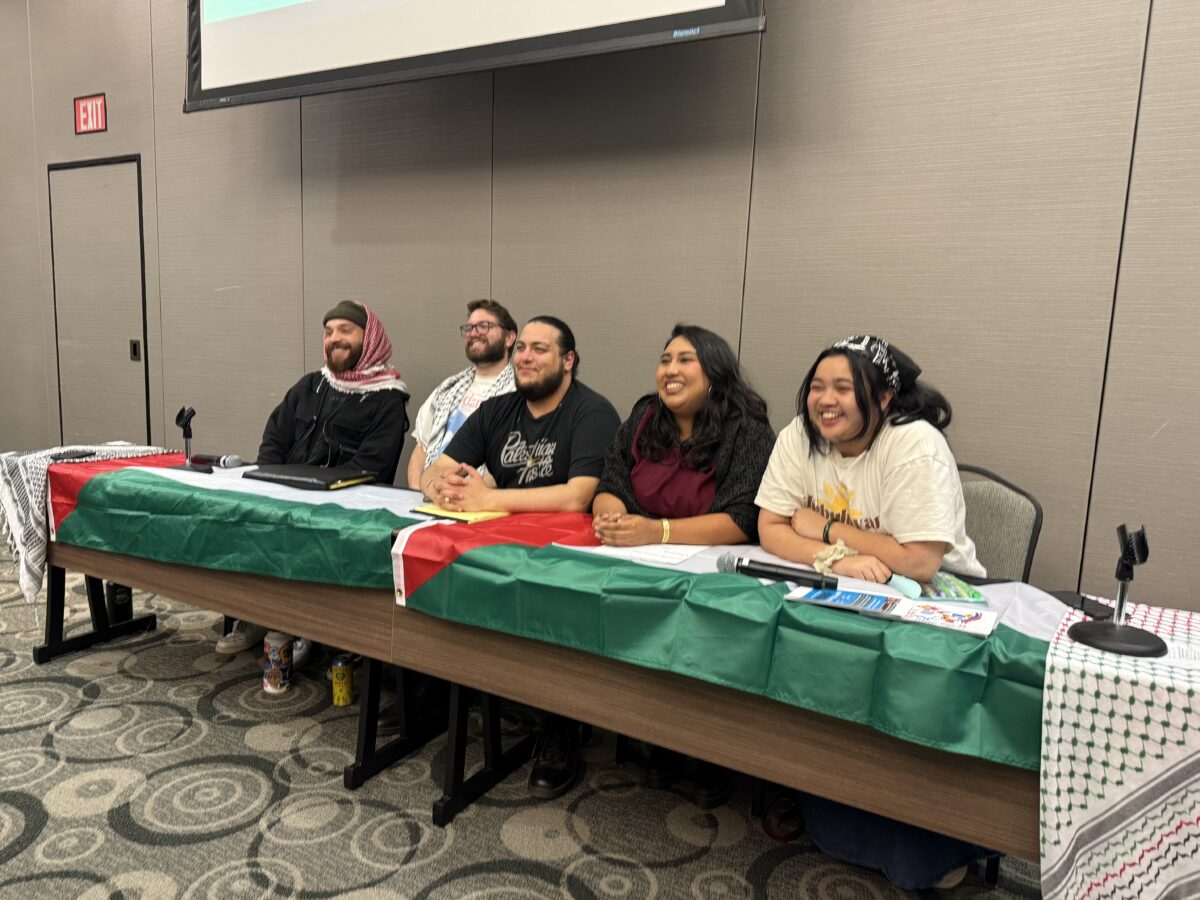 Five students in a conference room sitting at a table draped in a Palestinian flag.