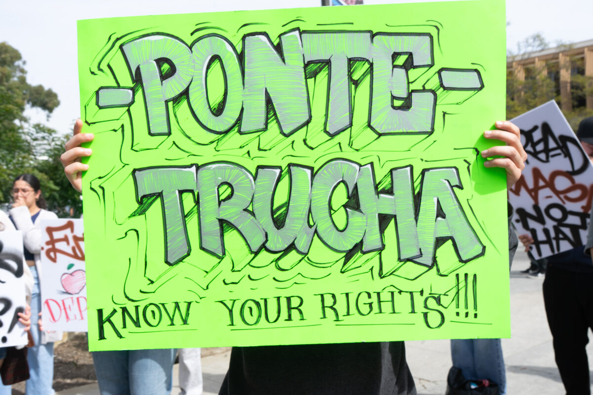 A student protester holds a neon green sign reading "PONTE-TRUCHA," OR "WATCH OUT" in Spanish.