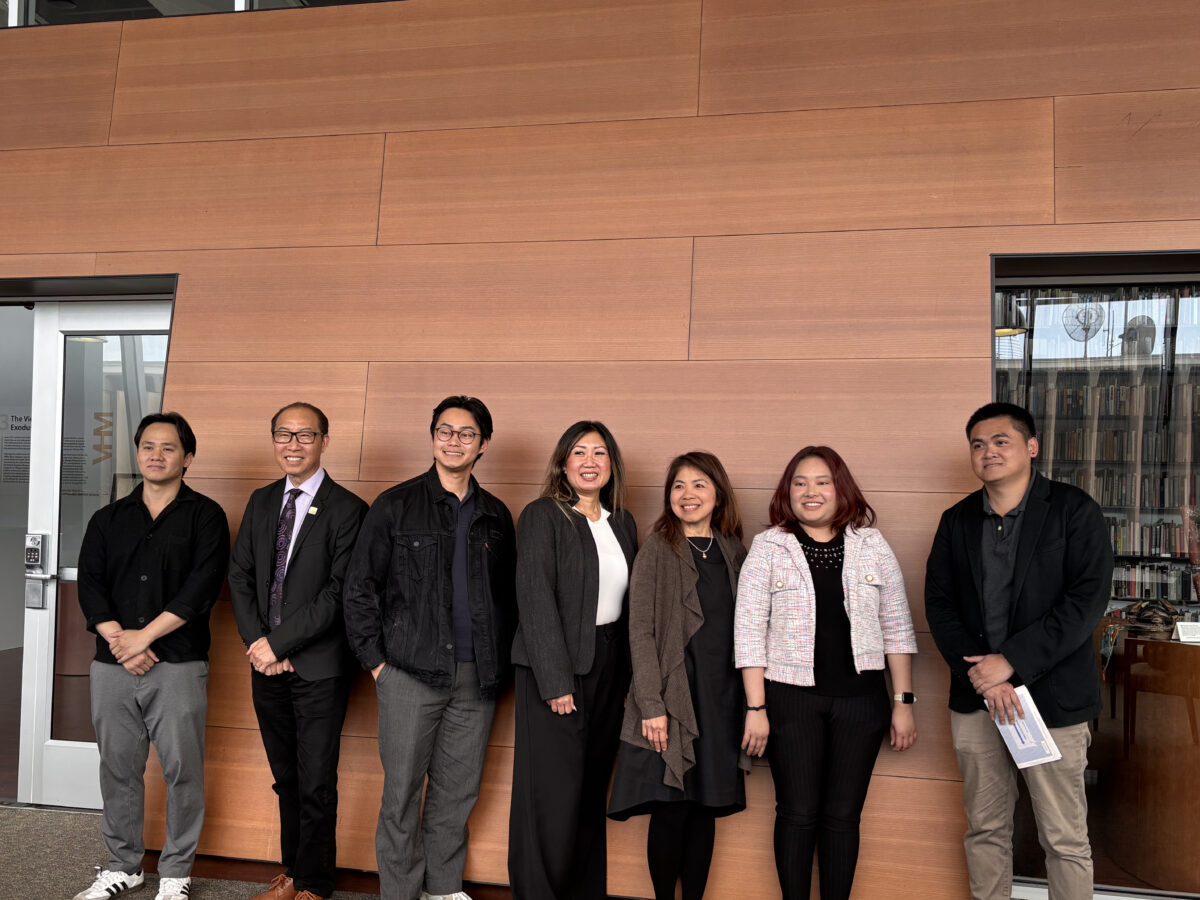 Seven speakers stand in a row against a wood-paneled wall at a Vietnamese American event, smiling after a panel discussion on migration, memory, and community resilience.